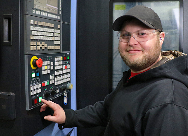 Man hitting a button on a panel while smiling at the camera