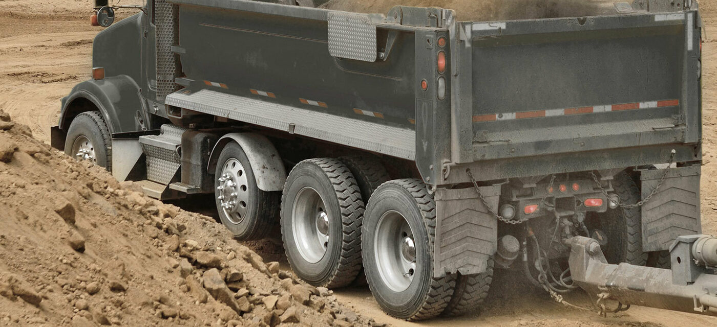 A dump truck with a link auxiliary axle on a worksite