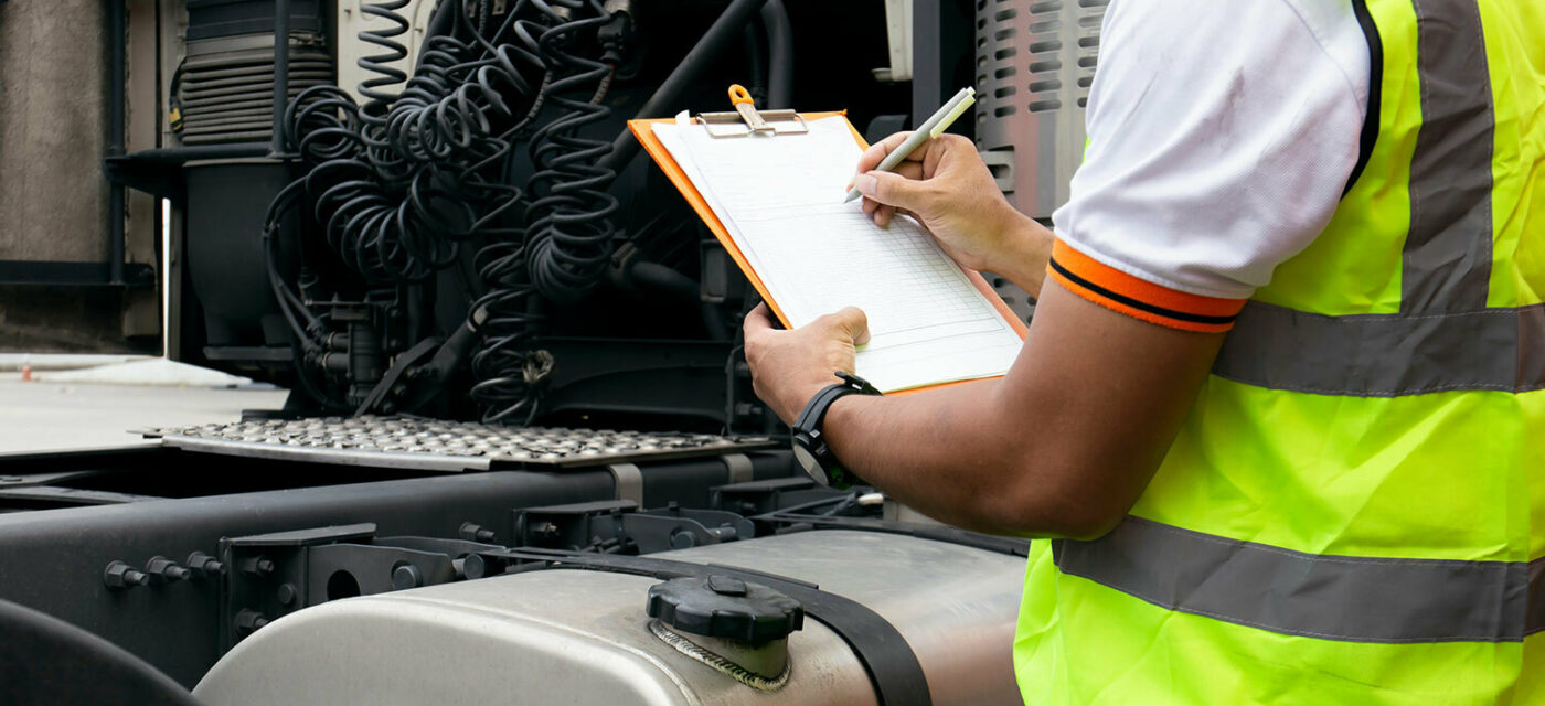 A man in a safety jacket marking a checklist by the rear of a semi truck cabin