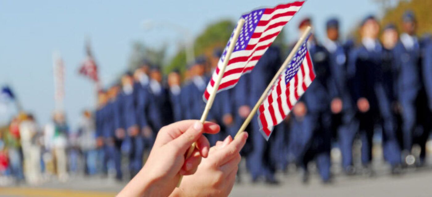 Two hands waving American flags at a Veterans' Day Parade