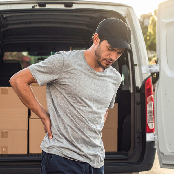 A man with a hand on his sore back looking down at the ground in pain.