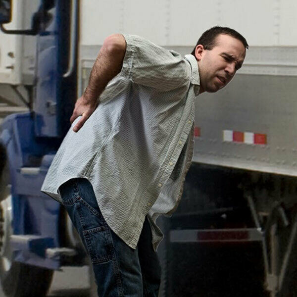 A man with a hand on his back indicating pain next to a landing gear on a truck trailer