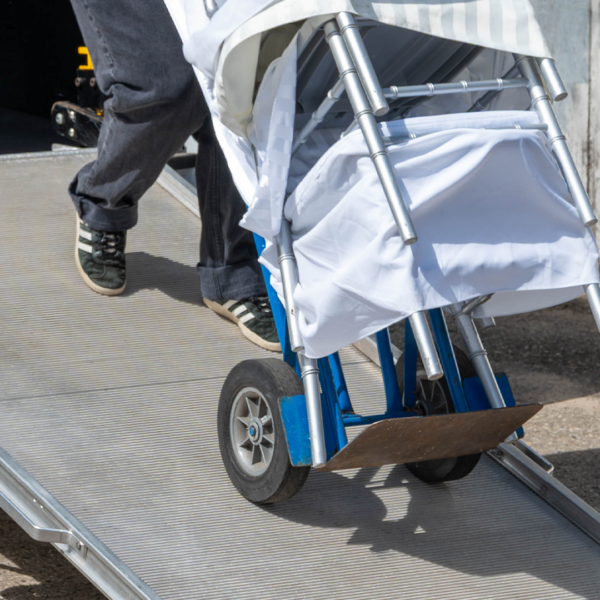 A person walking down a Link LSR90 Swivel Ramp with a dolly cart carrying covered chairs