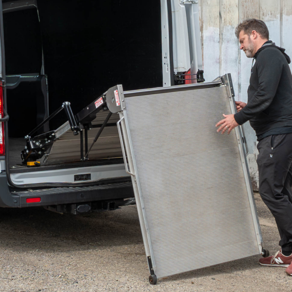 A man utilizing the LSR90 Swivel Ramp's spring assist feature and wheels over a gravel surface to easily stow it