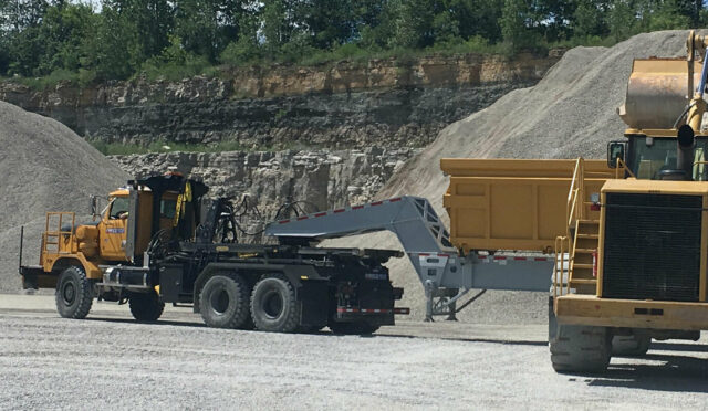 Work trucks in a quarry, one with a dump trailer.