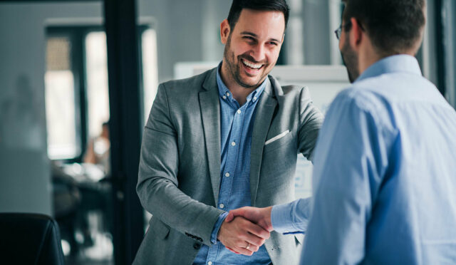 Two men shaking hands both dressed in blue button down shirts