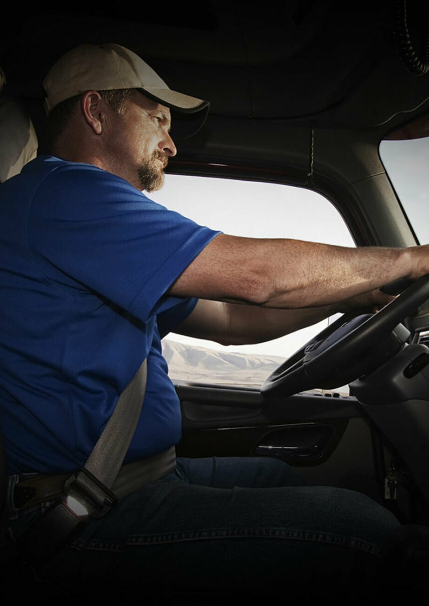 Low shot of a truck driver with his hands on the steering wheel looking out the windshield