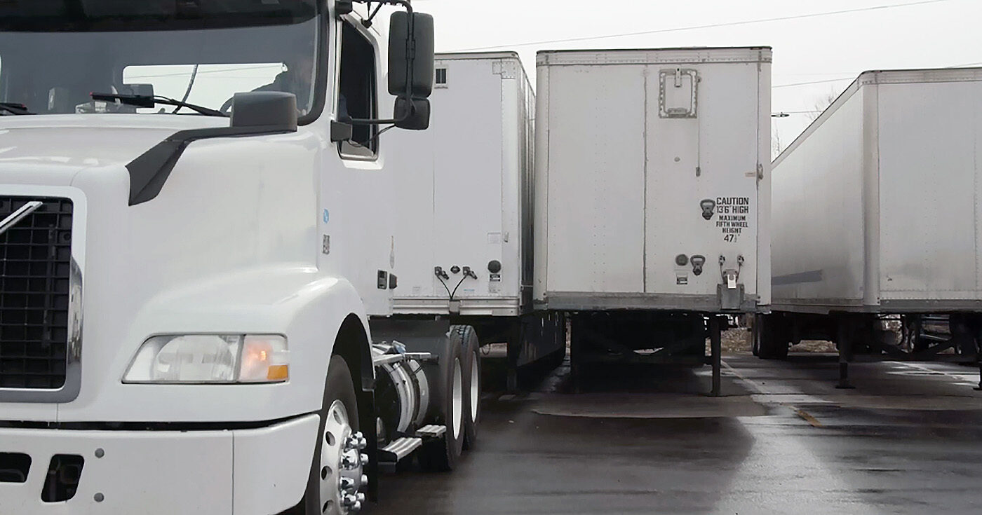 A truck that is backing up to connect to a trailer that is parked flush to another trailer.