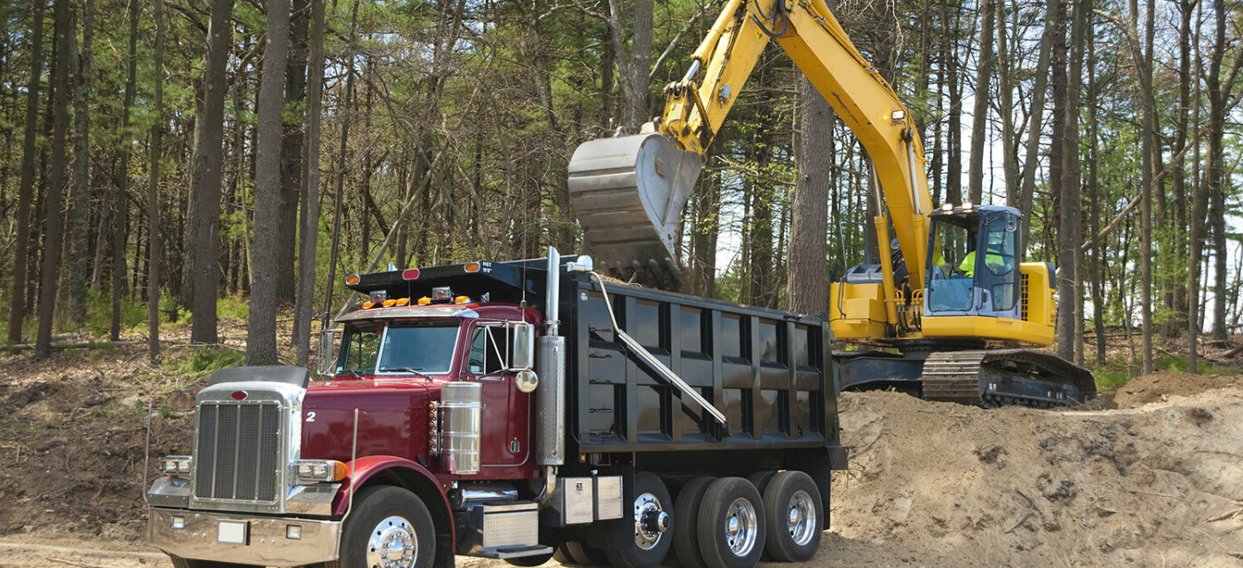 A dump truck equipped with a Link Auxiliary Suspension being loaded with dirt