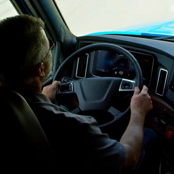 A driver behind the steering wheel of a semi truck looking out onto the road
