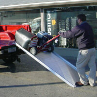 A man using a link portable ramp to unload equipment from the back of a pickup truck