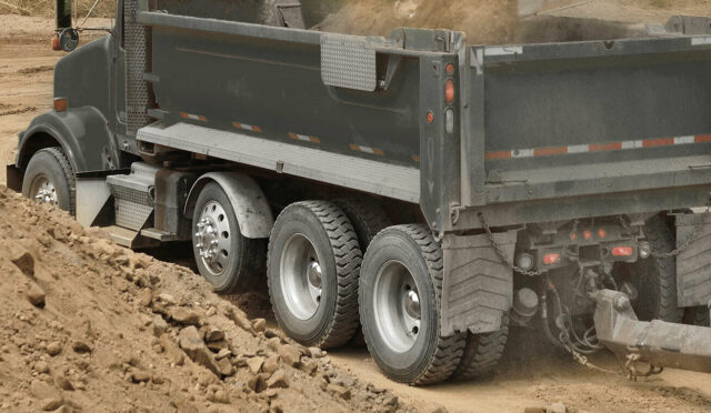 A dump truck with a link auxiliary axle on a worksite