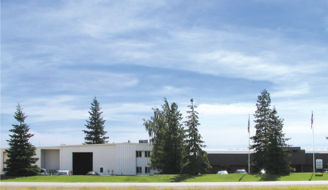 The exterior of Link Suspensions of Canada's headquarters; a building with pine trees in front of it