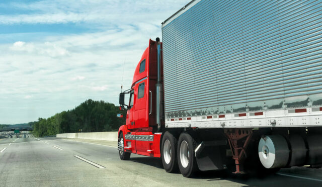 A red semi truck passing on the left with an enclosed trailer on a highway