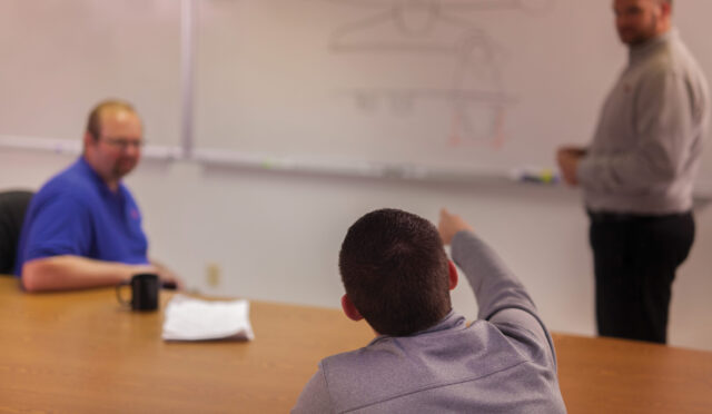 A Link engineer pointing at a drawn product on a whiteboard at an engineering meeting