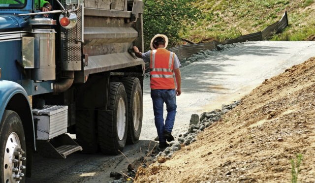 A man in an orange safety vest walking past a dump truck on a gravel road