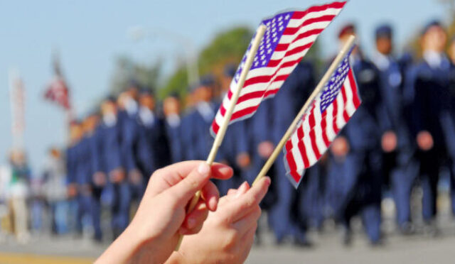 Two hands waving American flags at a Veterans' Day Parade