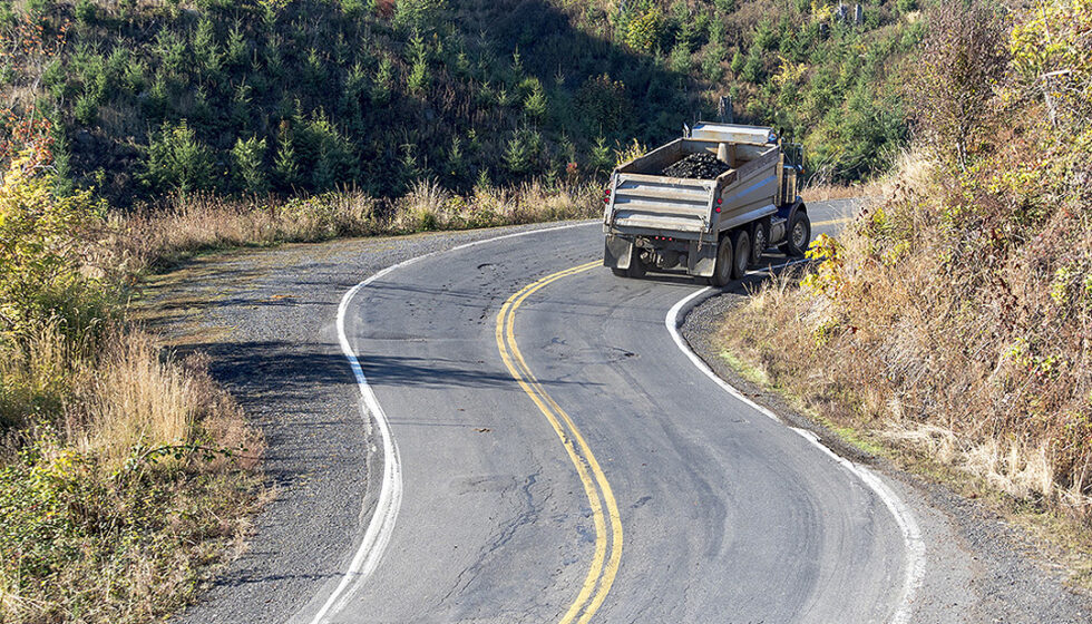 A dump truck driving on a winding, evergreen forest road.